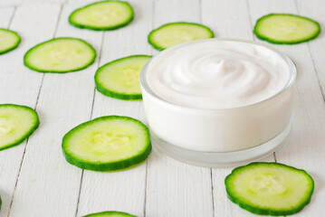 Moisturizer with cucumber slices on white wooden