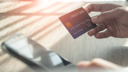 Woman hands holding a blue credit card and using a smartphone for shopping online or internet banking on wooden desk. Online shopping concept.