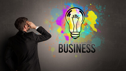 businessman drawing colorful light bulb with BUSINESS inscription on textured concrete wall, new business idea concept