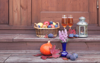 Obraz na płótnie Canvas Wicker basket with fruits, glasses of rose champagne, lantern, figs, pumpkin and purple spirea are on steps of rustic wooden ladder