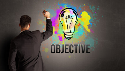 businessman drawing colorful light bulb with OBJECTIVE inscription on textured concrete wall, new business idea concept