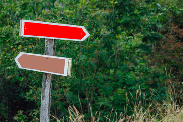 Directional arrow signs on wooden pole in the forest. Blank track pointers or guidepost against green nature background.