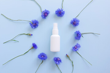 Mockup of unbranded white plastic spray bottle and floral frame of blue lowers on a pastel blue background. Natural organic spa cosmetics and liquid antimicrobial spray. Top view, floral flatlay.
