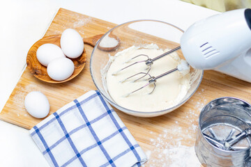 making dough for bread or homemade baked goods. ingredients on the desk. female hands hold a mixer for mixing dough