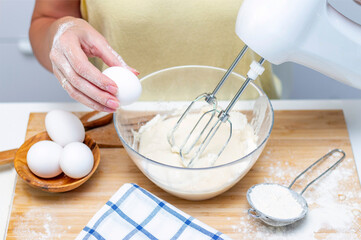 making dough for bread or homemade baked goods. ingredients on the desk. female hands holding an egg