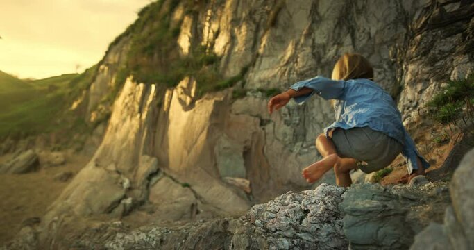 A preschooler is climbing a rock wall at sunset on the beach in summer