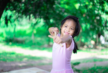 little asian girl shooting wooden slingshot against green tree background, active leisure for kids.