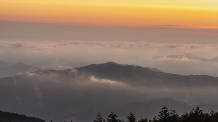 Zdjęcie przedstawia nadchodzący wschód słońca przeplatający się z piękną warstwą chmur widoczną ponad szczytami gór.