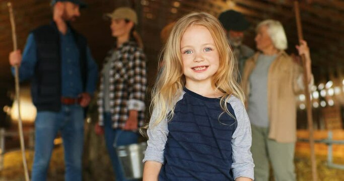 Portrait of cute Caucasian small girl smiling joyfully to camera in shed at village. Family on background. Parents and grandparents. Little beautiful cheerful child laughing in stable. Farming life.