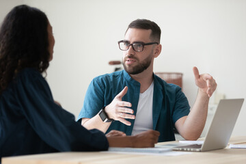 Confident businessman wearing glasses discussing project with colleague at meeting, sitting at...