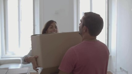 Happy man coming into room, carrying box with different stuff, kissing and hugging young wife. Attractive Caucasian couple moving into new apartment or house. Relocation, home and mortgage concept