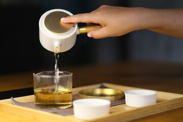 close up hand pouring tea water from traditional Chinese teapot to fair mug. Defocused background