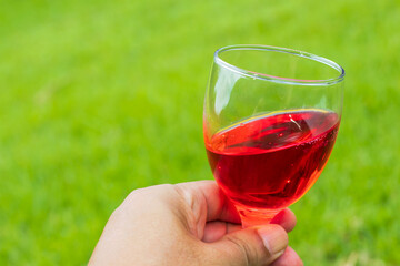 Close up hand holding a glass of red wine on natural background
