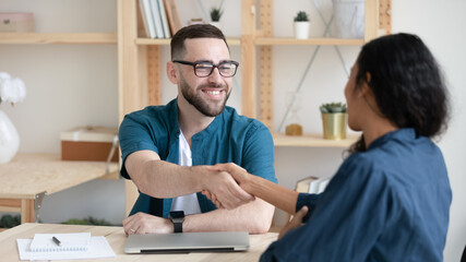 Smiling hr manager wearing glasses shaking African American candidate hand, greeting at meeting, congratulating after successful interview, good first impression, employment and hiring concept