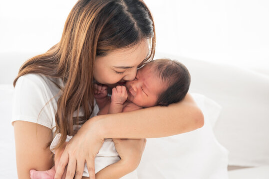 Pretty asian woman smile and holding a newborn baby in her arms. Happy family. Asia mother lifting and kiss her adorable infant baby on white. love people concept