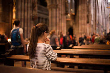 Girl in a church standing on her knees. Young religious woman in glasses with long dark hair,...