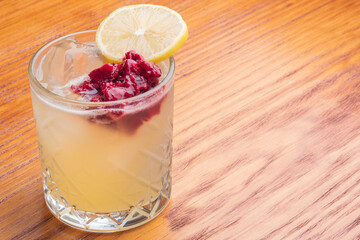 Yellow cocktail with lemon wedge and berries for garnish. Mixology cocktail in table