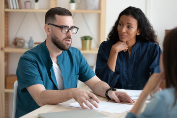 Obraz premium Serious businessman mentor wearing glasses speaking at meeting in modern boardroom, confident employee sharing ideas, diverse business partners discussing project, coach training staff