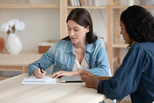 Confident businesswoman making notes at meeting, consulting African American client, hr manager holding job interview with candidate, business partners discussing contract terms, project strategy