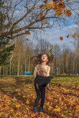 A cheerful girl throws up fallen leaves in the park.
