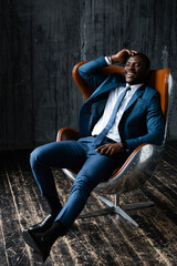 Man african american office worker in a blue suit resting in a loft armchair aviator