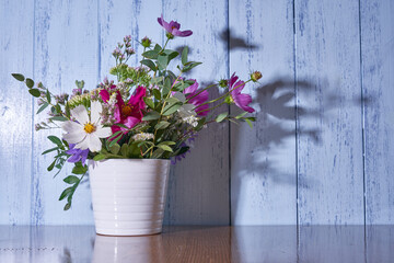  Multicolored wildflowers stand in a white vase against a blue wall 