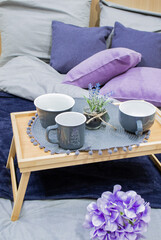 Fototapeta na wymiar The decor in the store: Breakfast in bed. Bed linen in blue-lilac tones, gray cups, napkin. Stylish interior
