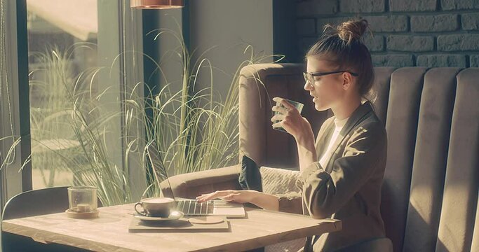 Woman working on tablet, sitting in cafe with glass of water. Girl in glasses pauses after work. Online chat with friends, long distance communication. Staying connected. 4K video
