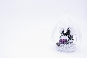 Transparent Christmas ball, inside which the figure of a house in a snowy forest among the firs. White background, copy space. Cozy winter holiday conception