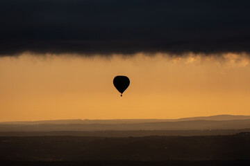In the low sun of the morning a balloon gets close to the cloud cover 