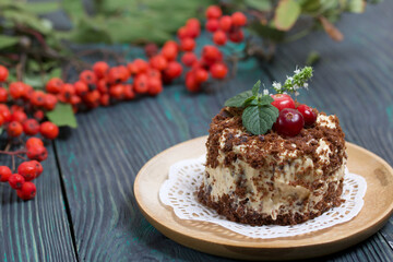 Sponge cake with butter cream. Decorated with cranberries and mint. Nearby are rowan branches with berries. Against the background of brushed pine boards.