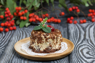 Sponge cake with butter cream. Decorated with cranberries and mint. Nearby are rowan branches with berries. Against the background of brushed pine boards.