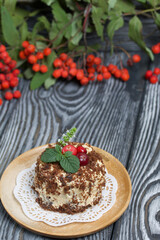 Sponge cake with butter cream. Decorated with cranberries and mint. Nearby are rowan branches with berries. Against the background of brushed pine boards.