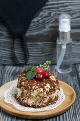 Sponge cake with butter cream. Decorated with cranberries and mint. Nearby is a protective mask and antiseptic. Against the background of brushed pine boards.