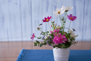 multicolored wildflowers stand on a wooden table, on a blue cloth napkin, in a white vase against a blue wall   