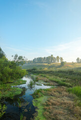 Tranquil hazy landscape with small river at sunrise