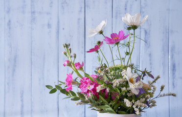 Close-up of multicolored wildflowers standing in a white vase against a blue wall   