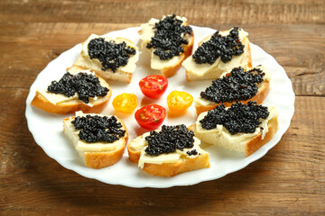 Sandwiches with black caviar on a white plate on a wooden table.