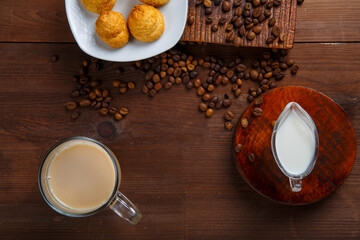 Fototapeta premium A mug with coffee with milk and a jug of cream and croissants on the table among the scattered coffee beans.