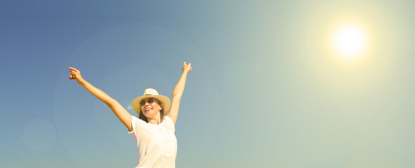 Fototapeta na wymiar Young cheerful woman raises her hands against the blue sky. The sun is shining