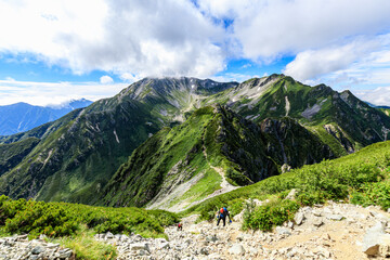 立山の広大な山脈と前剱の険しい岩場を登る登山者たち