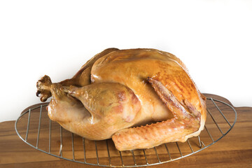 a stuffed roasted turkey in a wire rack on a wooden cutting board isolated on white