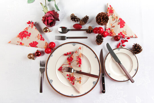 Overhead  View Of A Christmas Holiday Dinner Place Setting With Decorations And Pine Cones On A White Table Cloth