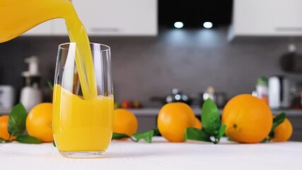 Orange juice pouring into glass on white table in modern kitchen. Citrus juice splash slow motion footage
