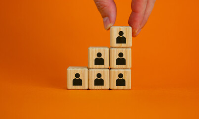 Business executive stacking wooden cubes with people icons on them in a pyramid shape in a...