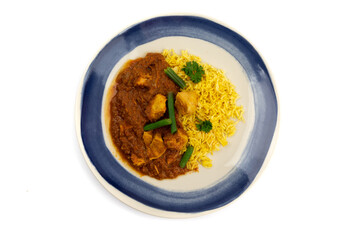 overhead view of a blue plate of Indian buttered chicken with green beans and curry rice isolated on a white background
