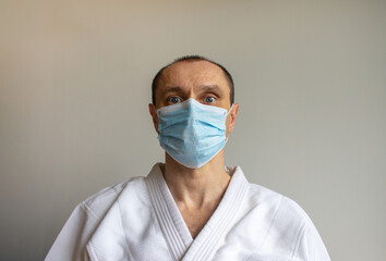 A young strong man in a white kimono with a blue medical mask. Emotion of fear. COVID-19 Pandemic Coronavirus concept.