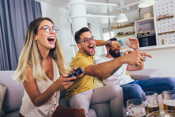Group of friends having fun sitting on sofa in living room and playing video games at home.