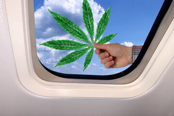 male hand with a green leaf of marijuana against the background of a beautiful heavenly landscape of blue sky with fluffy clouds behind the porthole of a plane, travel concept