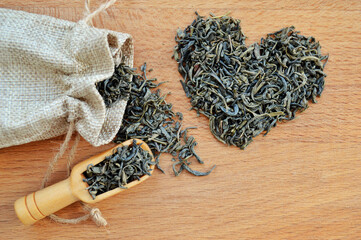 Heart made from loose leaf tea, jute bag and wooden spoon on wooden background.